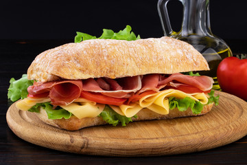Ciabatta sandwich with lettuce , prosciutto and  cheese on wooden board