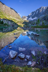Picturesque lake in the Altai Mountains. Beautiful reflection and stony shore. Morning light, rich colors.