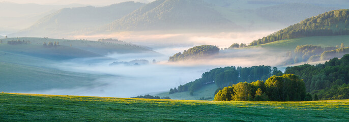 Panoramic view of a picturesque valley in the morning light. Fog, meadows and morning light. Spring rural landscape.