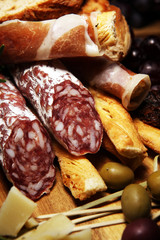 antipasto various appetizer. Cutting board with prosciutto, salami, cheese, bread and olives on dark wooden background