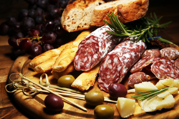 antipasto various appetizer. Cutting board with salami, cheese, bread and olives on dark wooden background