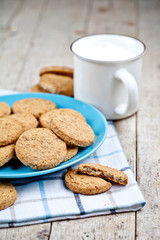 Fresh baked oat cookies on blue ceramic plate on linen napkin and cup of milk