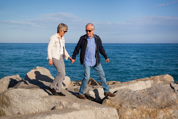 Active senior couple walking on sunny rocks by the sea