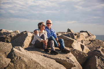 Fototapeta na wymiar Happy senior couple sitting on rocks by the sea