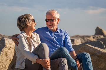 Happy senior couple sitting on rocks by the sea