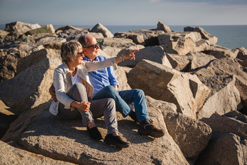 Happy senior couple sitting on rocks by the sea