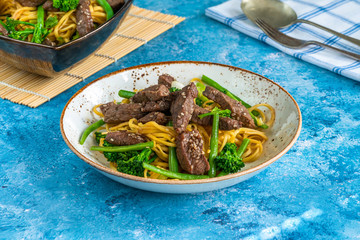 Honey and sesame beef noodles with green vegetables.