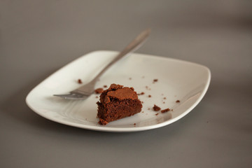 A white square plate with an almost eaten brown chocolate cake crumbs and a fork at the side.