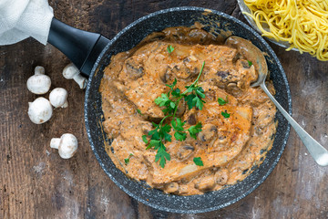 Pork chops in creamy cajun sauce with button mushrooms and parsley in a skillet - top view