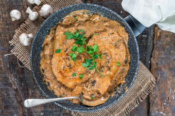 Pork chops in creamy cajun sauce with button mushrooms and parsley in a skillet - top view