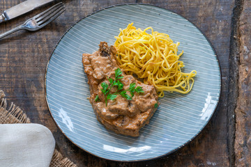 Pork chops in creamy cajun sauce with button mushrooms and egg noodles garnished with parsley - top view