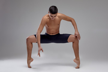 Photo of a handsome man ballet dancer, dressed in a black shorts, making a dance element against a...
