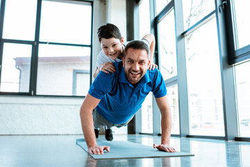 happy father doing push up exercise with son on back at gym