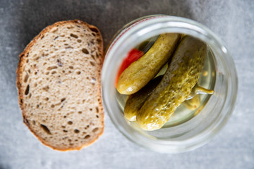 Ogórki w słoiku z papryczką, na betonowym tle wraz z bochenkiem chleba
