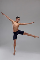 Fototapeta na wymiar Photo of a handsome man ballet dancer, dressed in a black shorts, making a dance element against a gray background in studio.