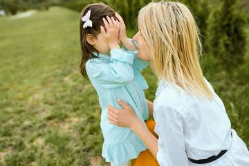 Fototapeta premium Pretty kid playing hide-and-seek with young mother outdoor. Portrait of joyful woman and her cute child playing in the park. Mother and daughter shares love. Happy Mothers Day. Motherhood, childhood