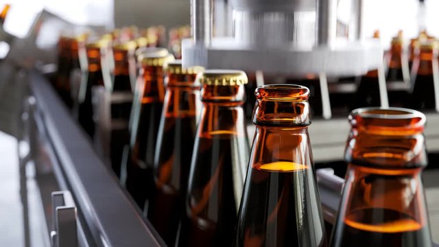 Glass bottles with liquid inside moving gradually in a factory pipeline. 4KHD