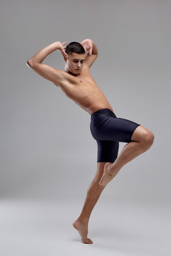 Photo of a handsome man ballet dancer, dressed in a black shorts, making a dance element against a gray background in studio. © nazarovsergey
