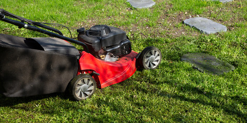 Red push lawn mower in Spring Summer season in grass green garden