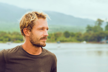 An attractive man on a lake shore near the mountains. Travel around Indonesia by a ferry boat. A...