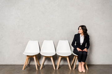 attractive brunette woman in formal wear sitting on chair before job interview