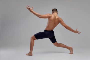 Photo of a handsome man ballet dancer, dressed in a black shorts, making a dance element against a gray background in studio.