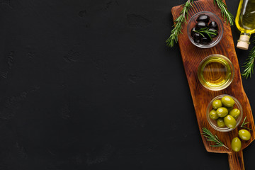 Olive oil and olives in bowls on black.