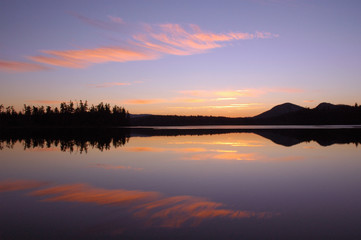 Fototapeta na wymiar Sunset over Barnum Pond in the Adirondack Mountains with sky and mountains reflecting in calm water