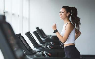 Young woman exercising on treadmill and listening music