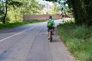 The guy rides a bike on the road in the summer - rear view.