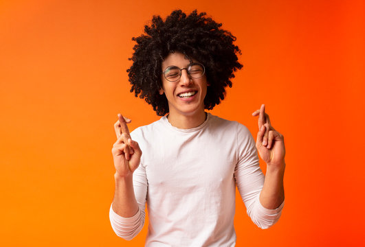 Cheerful black guy crossing fingers for luck