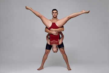 The couple of an athletic modern ballet dancers are posing against a gray studio background.