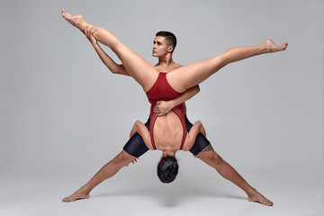 Obraz premium The couple of an athletic modern ballet dancers are posing against a gray studio background.