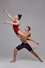 Fototapeta na wymiar The couple of an athletic modern ballet dancers are posing against a gray studio background.