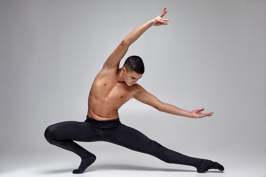 Photo of an athletic man ballet dancer, dressed in a black tights and pointe, making a dance element against a gray background in studio.