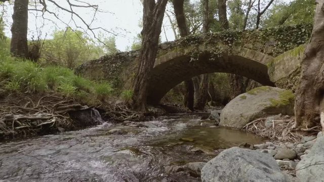 Slow motion handheld shot of river flowing under a medieval bridge in Cyprus
