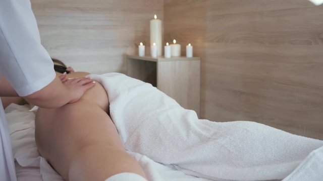 Young woman having anticellulite buttock massage in the beauty spa salon. Masseuse makes cellulite massage to a young beautiful girl on the background of a candle. Medium shot