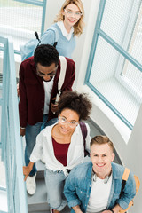 Fototapeta na wymiar Overhead view of four smiling multiethnic students with backpacks on stairs