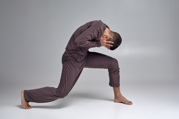 Photo of an athletic man ballet dancer dressed in a gray tracksuit, making a dance element against a gray background in studio.