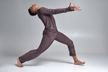 Photo of an athletic man ballet dancer dressed in a gray tracksuit, making a dance element against a gray background in studio.