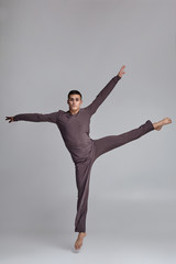 Photo of an athletic man ballet dancer dressed in a gray tracksuit, making a dance element against...
