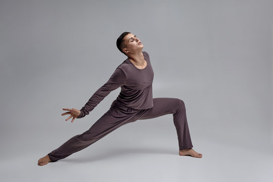 Photo of an athletic man ballet dancer dressed in a gray tracksuit, making a dance element against a gray background in studio. - Powered by Adobe