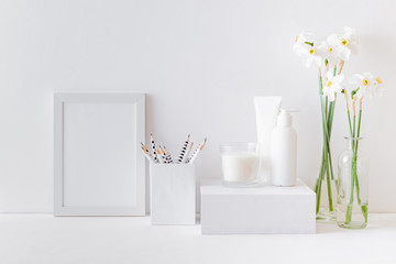 Home interior with decor elements. White frame, white daffodils in a vase, cosmetic set