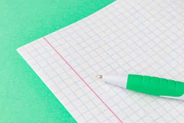 The concept of preparation for school. Pen closeup on notebook sheet in a cage. Background image for training topics, school lessons. Place for text.