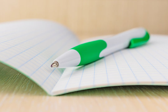 The concept of preparation for school. Pen closeup on notebook sheet in a cage. Background image for training topics, school lessons. Place for text.
