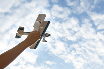 Children's hand holds a toy plane against the sky,blue sky white clouds