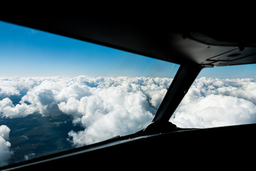 Pilots view out of the cockpit window toward clouds and blue sky above 