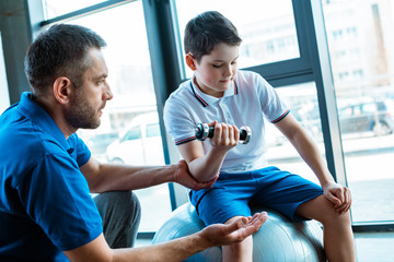 Obraz premium handsome father helping son exercising with dumbbell at gym