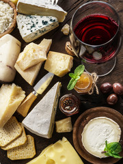 Cheese platter with organic cheeses, fruits, nuts and wine on wooden background. Top view. Tasty cheese starter.