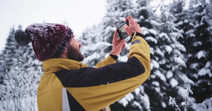 Young tourist taking pictures of a snowy forest in the winter day , he are very impressed by the all beauty he see around him